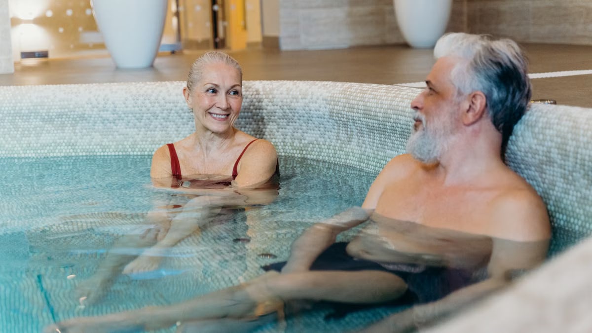 Smiling senior couple relaxing together in an indoor spa pool, enjoying leisure time.